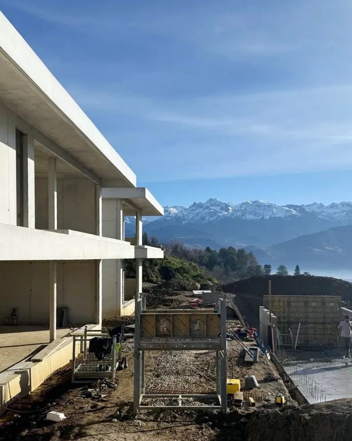 Maison moderne en béton, en phase de construction, avec vue sur les Alpes